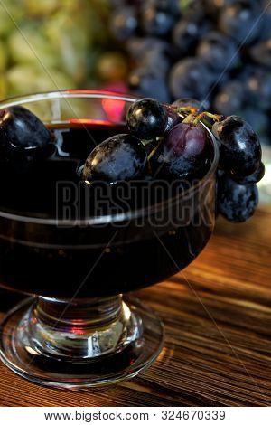 Wide Glass With Homemade Wine, Tincture Or Juice Next To Red And Black Grapes On The Background Of M