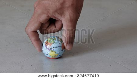 Fingers Grabbing A Small Globe With Grey Concrete Background Seen From The Front. World In Our Hands