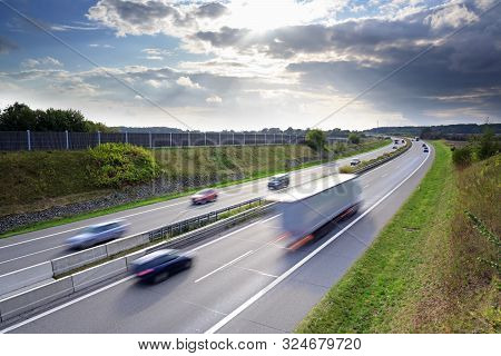 Highway In The Country With Driving Cars And Trucks In Motion Blur Under A Dramatic Sky With Clouds,