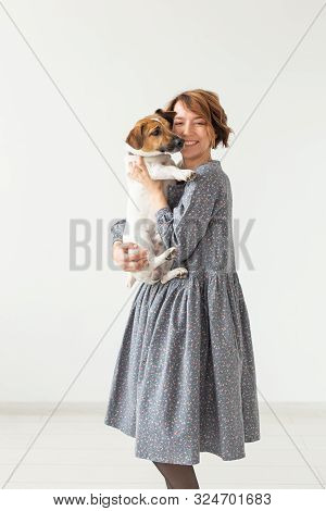 Charming Smiling Young Woman In A Stylish Gray Dress Holding Her Favorite Dog Jack Russell Terrier. 