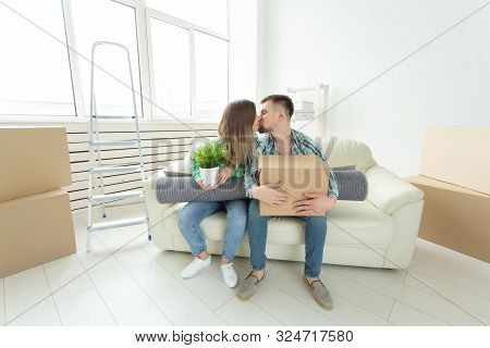 Moving And Real Estate Concept - Happy Couple Kissing On Sofa In Their New Flat