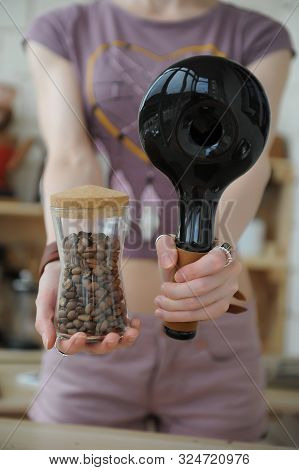 Girl Holds In Hands Ceramic Sample Coffee Roaster And Glass Jar With Freshly Roasted Coffee Beans