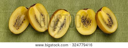 row of cut gold kiwifruit berries against green textured paper, long banner format