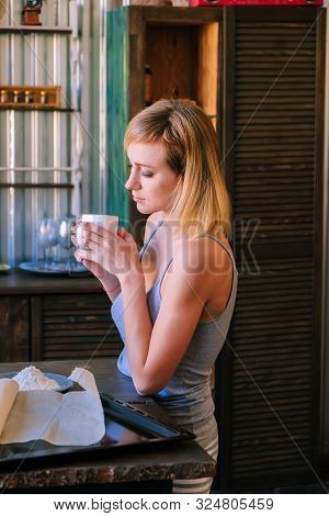 A Beautiful Freckled Blonde Girl In Pajamas Is Standing Near The Kitchen Table, Drinking Fock, Tea A