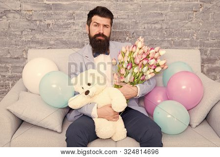 Best Boyfriend Ever. Romantic Man With Flowers And Teddy Bear Sit On Couch Waiting Girlfriend. Roman
