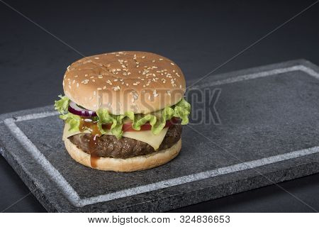 Hamburger With A Double Serving Of Meat, Tomatoes, Salad, Onions On A Wooden Board In A Restaurant.c