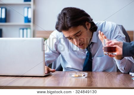Male employee drinking alcohol and smoking cigarettes at workpla