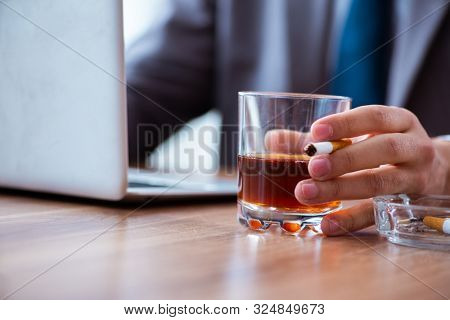 Male employee drinking alcohol and smoking cigarettes at workpla