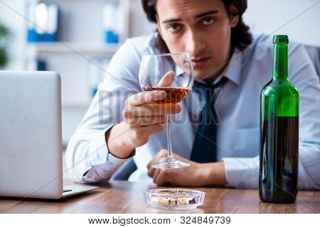 Male employee drinking alcohol and smoking cigarettes at workpla