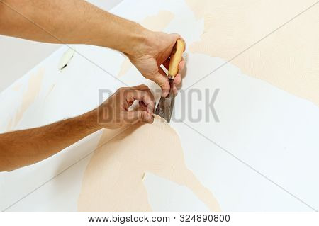 Close-up View On Hands With A Scraper In The Process Of Removing Old Wallpaper. Preparing The Wall F