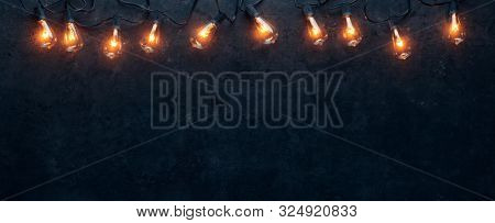 Row of lit string light bulbs glowing on dark grungy background.