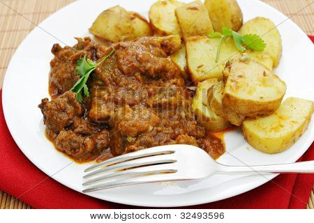Madras Butter Rindfleisch Curry serviert mit Curry-Kartoffeln und mit Koriander-Blättern garniert