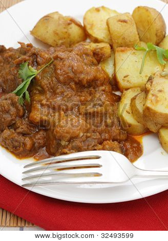 Verlässt ein Madras Butter-Rindfleisch-Curry mit Koriander garniert und serviert mit Curry-Kartoffeln