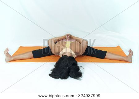 A Dark Haired Woman Is On An Orange Exercise Mat On White Background In Forward Fold, Reverse Prayer