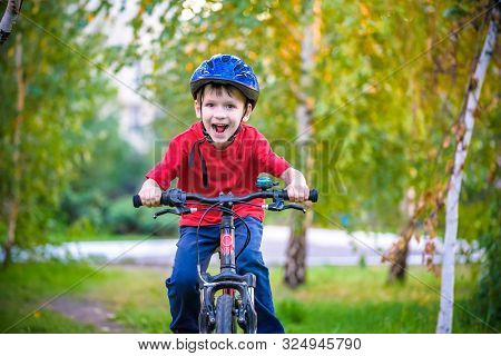 A Small White Toddler Boy In A Protective Helmet On His Head Sits On A Children's Bicycle. Toddler O