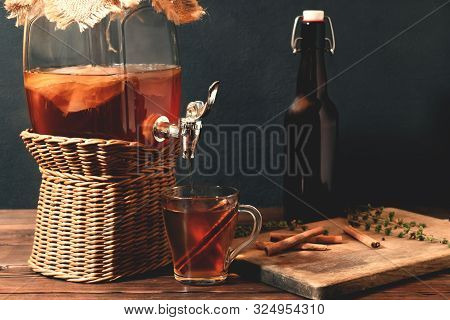 Fresh Homemade Kombucha Fermented Tea Drink In Jar With Faucet And In Cup And Bottle On Black Backgr