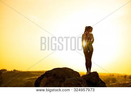 Young Beautiful Woman Standing on the Rock Against a Hot Beautiful Summer Sunset. Adventure and Healthy Active Lifesyle Concept.