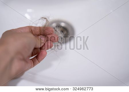 Woman Hand Is Holding Shred Of Hair Fallen To Bathroom Sink.