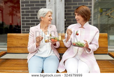 old age, leisure and food concept - senior women or friends eating takeaway salad on city street
