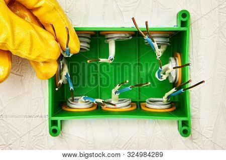 An Electrician In Yellow Protective Gloves Connects The Conduit To A Square Electrical Junction Box 