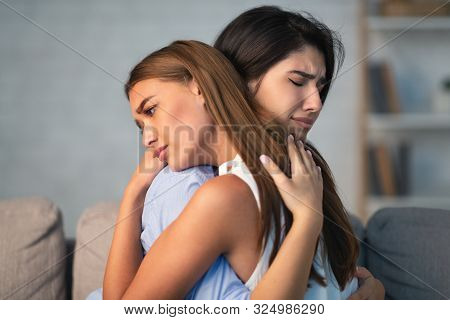 Compassionate Girl Hugging Crying Friend Supporting Her After Breakup With Boyfriend Sitting On Sofa
