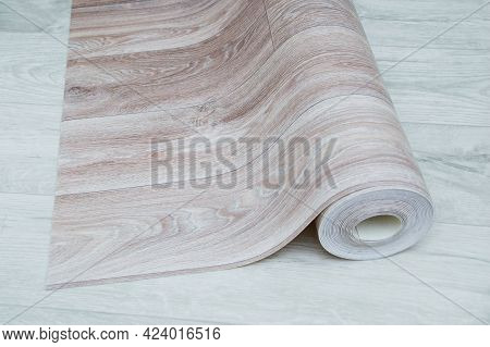 Unwound Roll Of Beige Linoleum With Wood Texture On A White Wooden Floor.