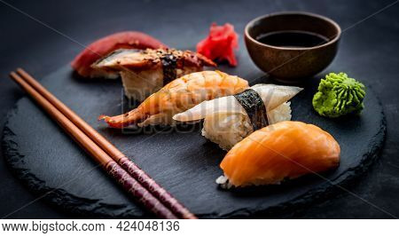 Tasty sushi sashimi set composition with shrimps, ginger and soy sauce served with chopsticks and green wasabi on black round plate. Traditional asian food with rice and seafood