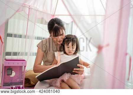 Asian Beautiful Loving Mother Read Storytale To Young Little Girl Daughter In Tent At Home. Parent P