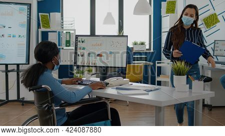 Paralysed Black Businesswoman And Employee With Protective Mask Working Together At Financial Projec