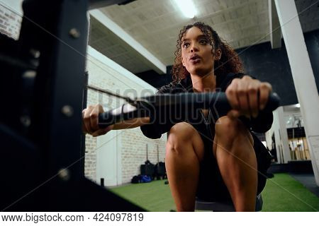 African American Female Using A Rowing Machine During Cross Fit Training. Female Athlete Exercising 