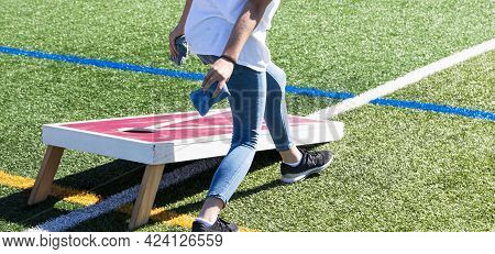Rear View Of People Playing Cornhole With Homemade Wood Boards On A Green Turf Field.