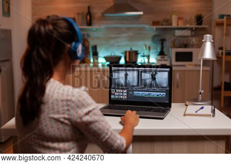 Brunette Video Editor Works With Footage On Personal Laptop In Home Ktichen During Night Time. Conte