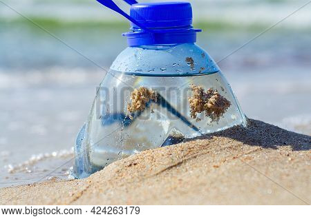 Plastic Bottle In Beach Sand. Plastic Pollution Of The Oceans Concept. Package Garbage On The Shore.