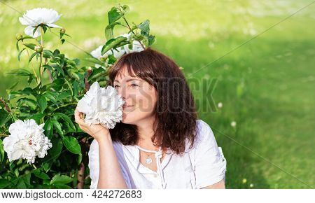 Portrait Nice Woman Of Forty Five Years Old With Brown Hair Sitting On Green Lawn In Sun And Sniffs 