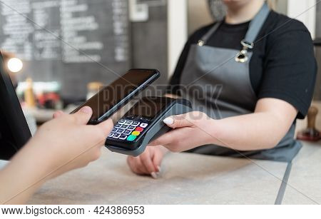 A Woman Pays With A Phone With Nfs Technology On The Phone With A Contactless Terminal In A Cafe Sho