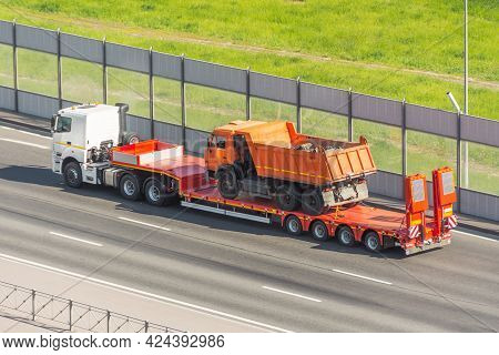 Orange Truck Dump With A Load Of Soil In The Body, Transported On A Trailer To The Loading Platform 