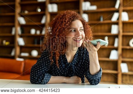 Smiling Young Redhead Woman Using Convert Voice Into Text Mobile App, Holding Smartphone And Talking