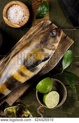 Raw Fish Sea Bass Or Lingcod And Seasonings For Cooking It On A Wooden Background Top View, Vertical