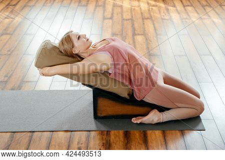 Mature Woman Doing Stretching Exercises On Yoga Backbend Bench In Studio
