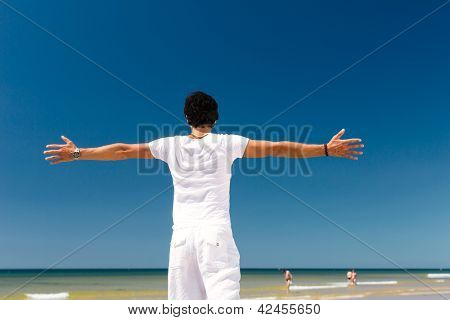 Stilig man på havet stranden njuter av sin semester, armar som sträcks ut mot solen som 