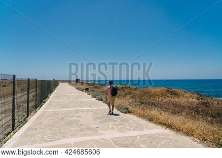 Theme Of Exploring Island Of Cyprus On Foot. Man With A Backpack Is Walks Along The Sea By Coastal B