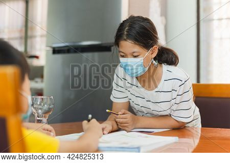 Asian Sister In Protective Mask Teaching Younger Brother Homework.