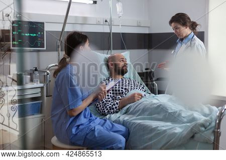 Patient Talking With Doctors While Resting In Bed During Disease Recovery In Hospital Ward. Practiti