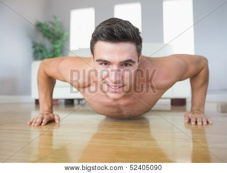 Happy handsome man doing push ups in bright living room