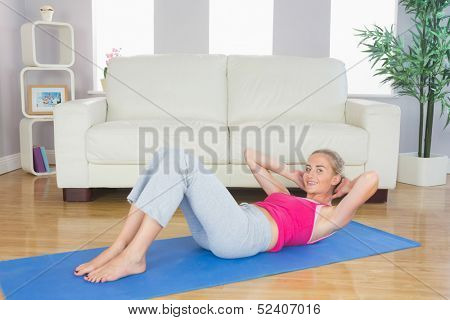Sporty happy blonde doing sit ups in bright living room