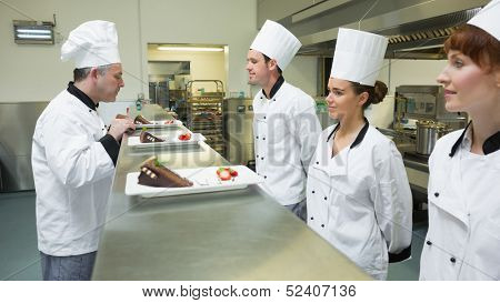 Three chefs presenting their plates to the head chef in a kitchen