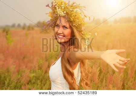 Portrait of a romantic smiling young woman in a circlet of flowers outdoors.