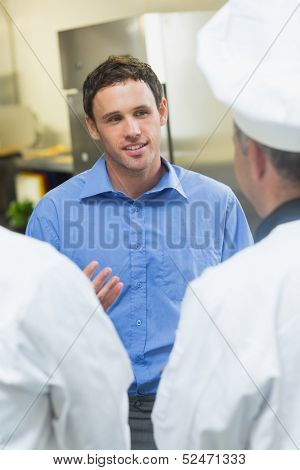 Young manager talking to the staff standing in a kitchen