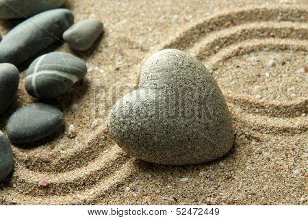 Grey zen stone in shape of heart, on sand background