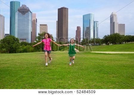 Two sister girls friends running holding hand in urban modern skyline on grass lawn